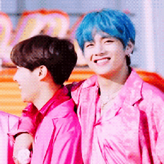 a man with blue hair is standing next to another man in pink shirts .