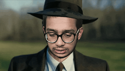 a man wearing a hat and glasses looks down at something