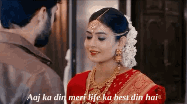 a man and a woman are standing next to each other and the woman is wearing a red saree and gold jewelry .