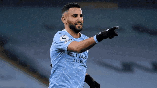 a soccer player wearing a blue etihad airways jersey points at something