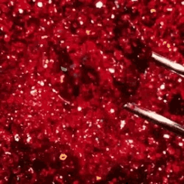 a close up of red glitter with tweezers in it .