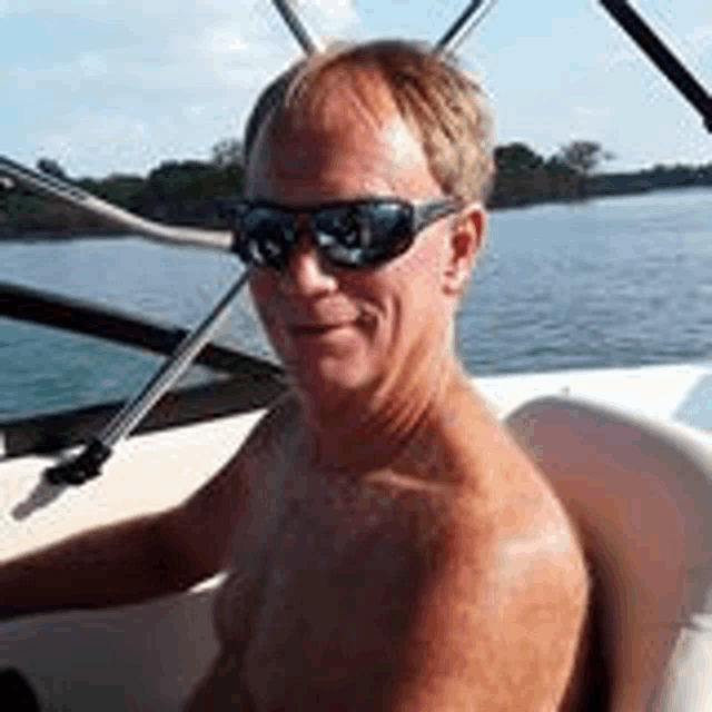 a shirtless man wearing sunglasses is sitting on a boat on a lake .