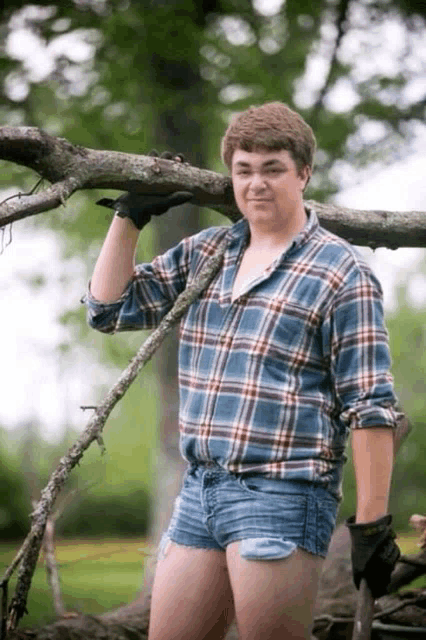 a man in shorts and a plaid shirt holds a tree branch