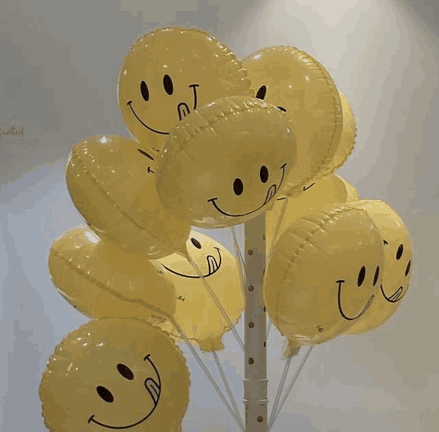 a bunch of yellow smiley face balloons hanging from a pole