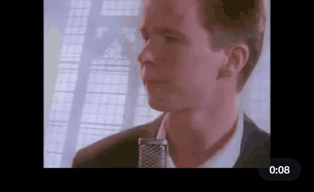 a man in a suit and tie is singing into a microphone in front of a window .