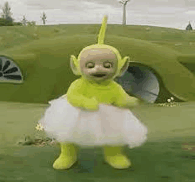 a yellow teletubbies doll is dancing in a tutu in a field .