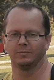 a man wearing glasses is looking at the camera with a serious look on his face .