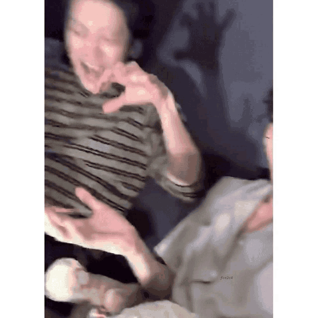 a blurry picture of two people making a heart shape with their hands while sitting on a couch .