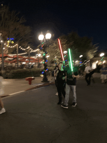 a couple of people walking down the street with lightsabers