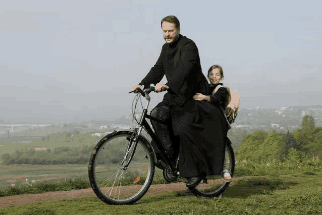 a man in a black robe is riding a bicycle with a little girl on the back