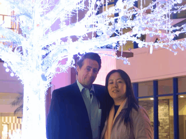 a man and a woman are posing for a picture in front of a tree