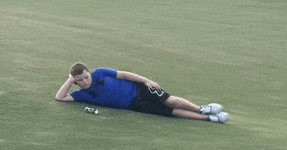 a man in a blue shirt and black shorts is laying on the grass with his legs crossed