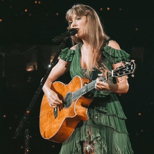 a woman in a green dress is playing a guitar