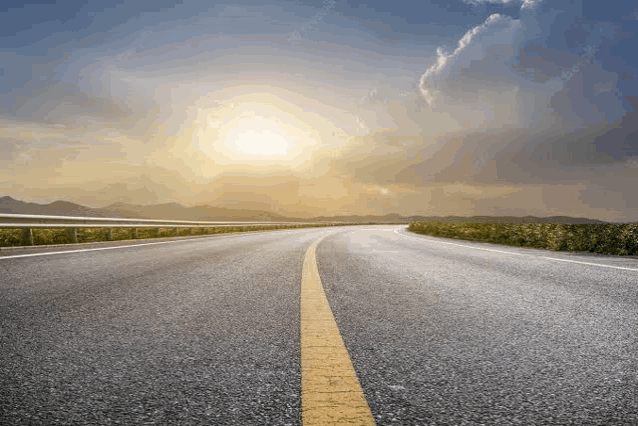 a road with the sun shining through the clouds on the horizon