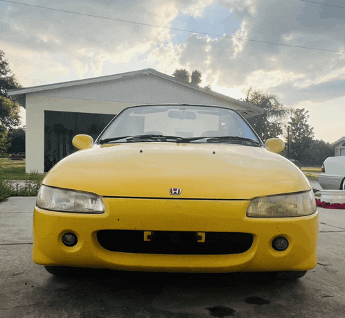 a yellow honda car is parked in front of a house