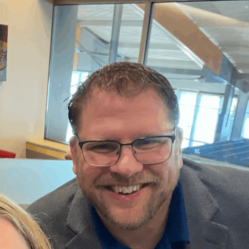 a man wearing glasses and a blue shirt is smiling