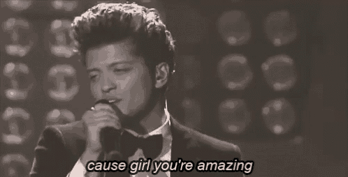 a man in a tuxedo singing into a microphone with the words " cause girl you 're amazing " below him