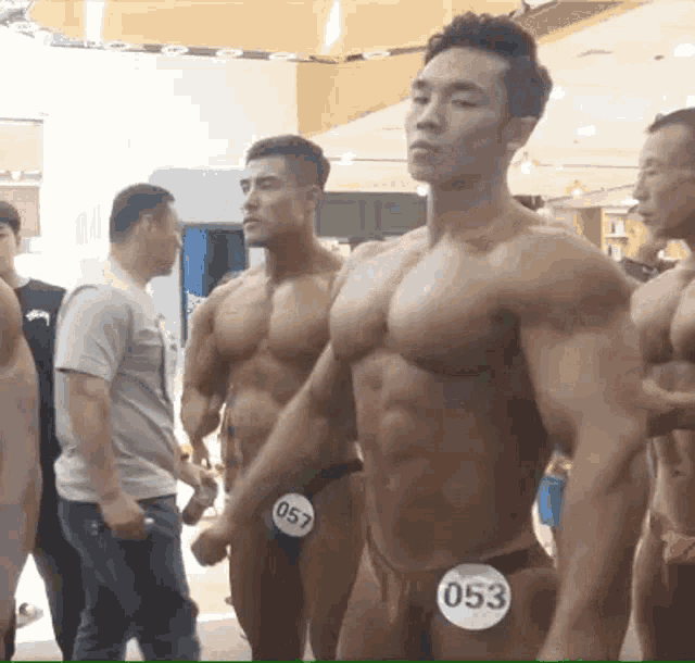 a group of muscular men are standing next to each other in a room .