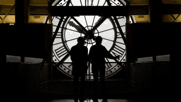 two men are standing in front of a large clock tower .