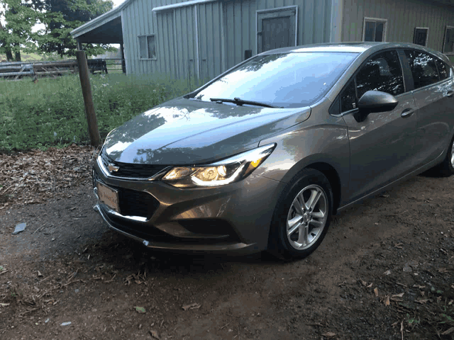 a grey chevrolet car is parked in front of a green barn