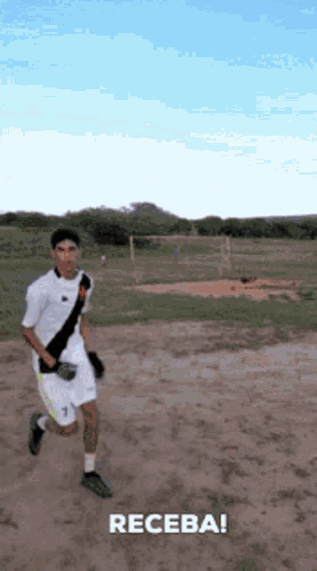 a man in a white shirt and shorts is running on a dirt field with the word receba written below him