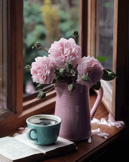 a cup of coffee sits next to a vase of flowers on a window sill