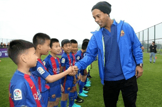 a man in a blue jacket shakes hands with a group of young boys wearing qatar shirts