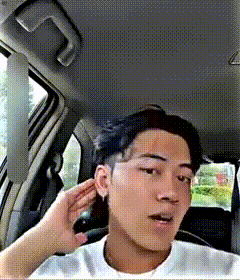 a man in a white shirt is sitting in a car with his hand on his ear .