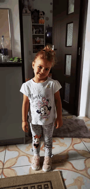 a little girl wearing a minnie mouse shirt stands in front of a door