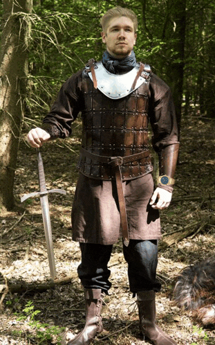 a man in leather armor holds a sword in the woods