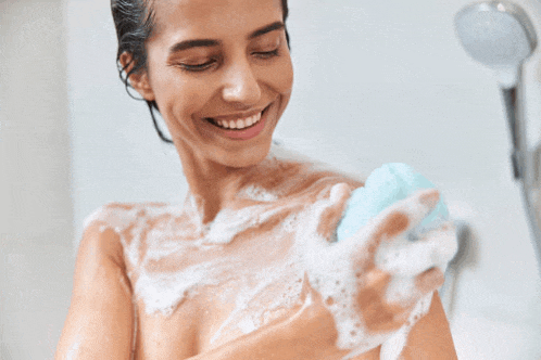 a woman is taking a shower and smiling while holding a soap bar