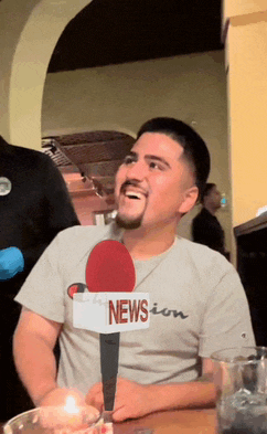 a man wearing a champion shirt is holding a microphone that says news