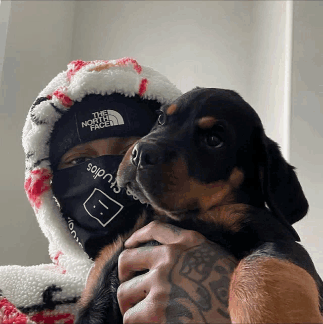 a man wearing a bandana that says the north face holds a puppy