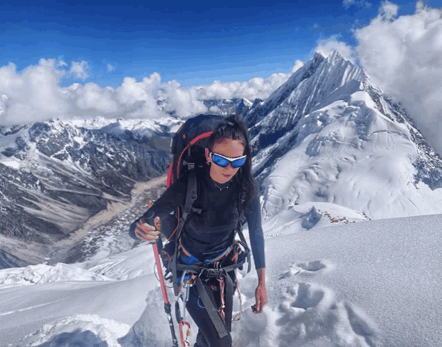 a woman wearing sunglasses and a backpack is walking on top of a snowy mountain