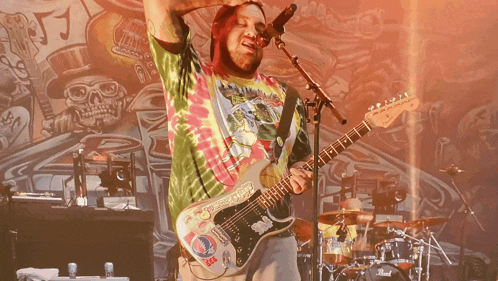 a man in a tie dye shirt playing a guitar