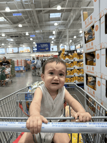 a baby sits in a shopping cart in front of a sign that says 1,000 on it