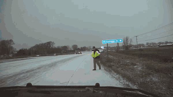 a man in a yellow vest stands on the side of a snowy road near a sign that says winterhage dr.