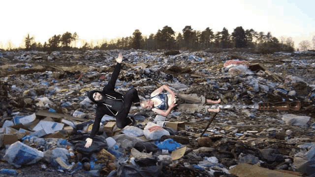 two people are laying in a pile of garbage and one of them is wearing a black hoodie