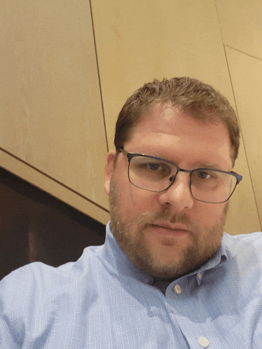 a man wearing glasses and a blue shirt is looking at the camera