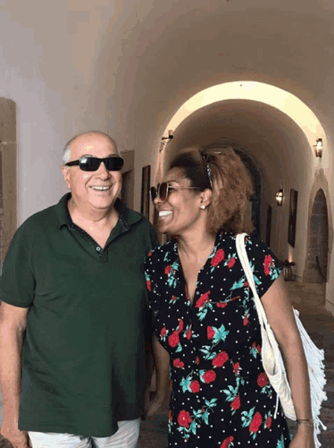 a man wearing sunglasses and a woman wearing a floral dress smile for the camera