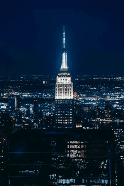 the empire state building is lit up at night with a city in the background