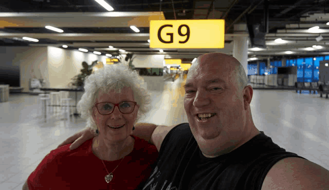 a man and woman are posing for a photo in front of a sign that says g9