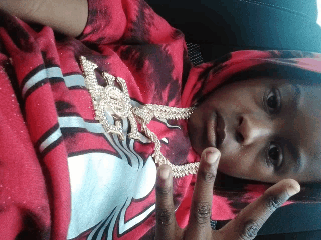 a person wearing a red tie dye shirt and a gold necklace giving the middle finger