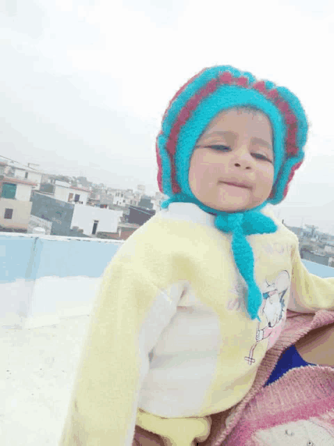 a baby wearing a blue and red hat and a yellow sweater with a cat on it