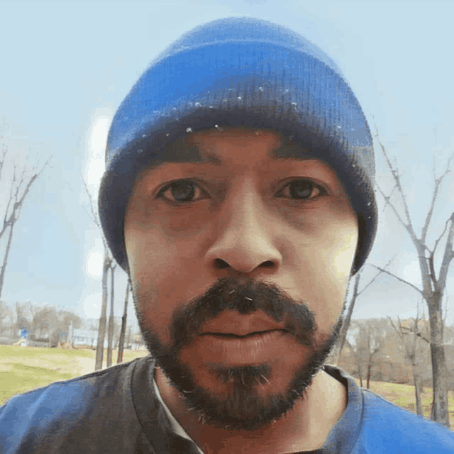 a man with a beard wearing a blue beanie looks at the camera