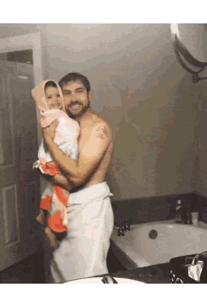 a shirtless man is holding a little girl in a bathroom