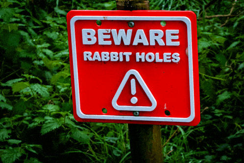 a red sign says beware rabbit holes in white letters