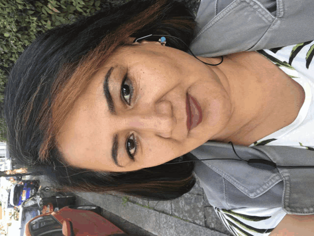 a close up of a woman 's face with a red car parked in the background