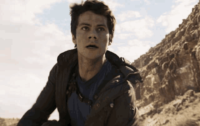 a young man in a brown jacket and blue shirt is standing in the desert