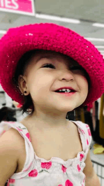 a little girl wearing a pink hat and a white dress is smiling at the camera .